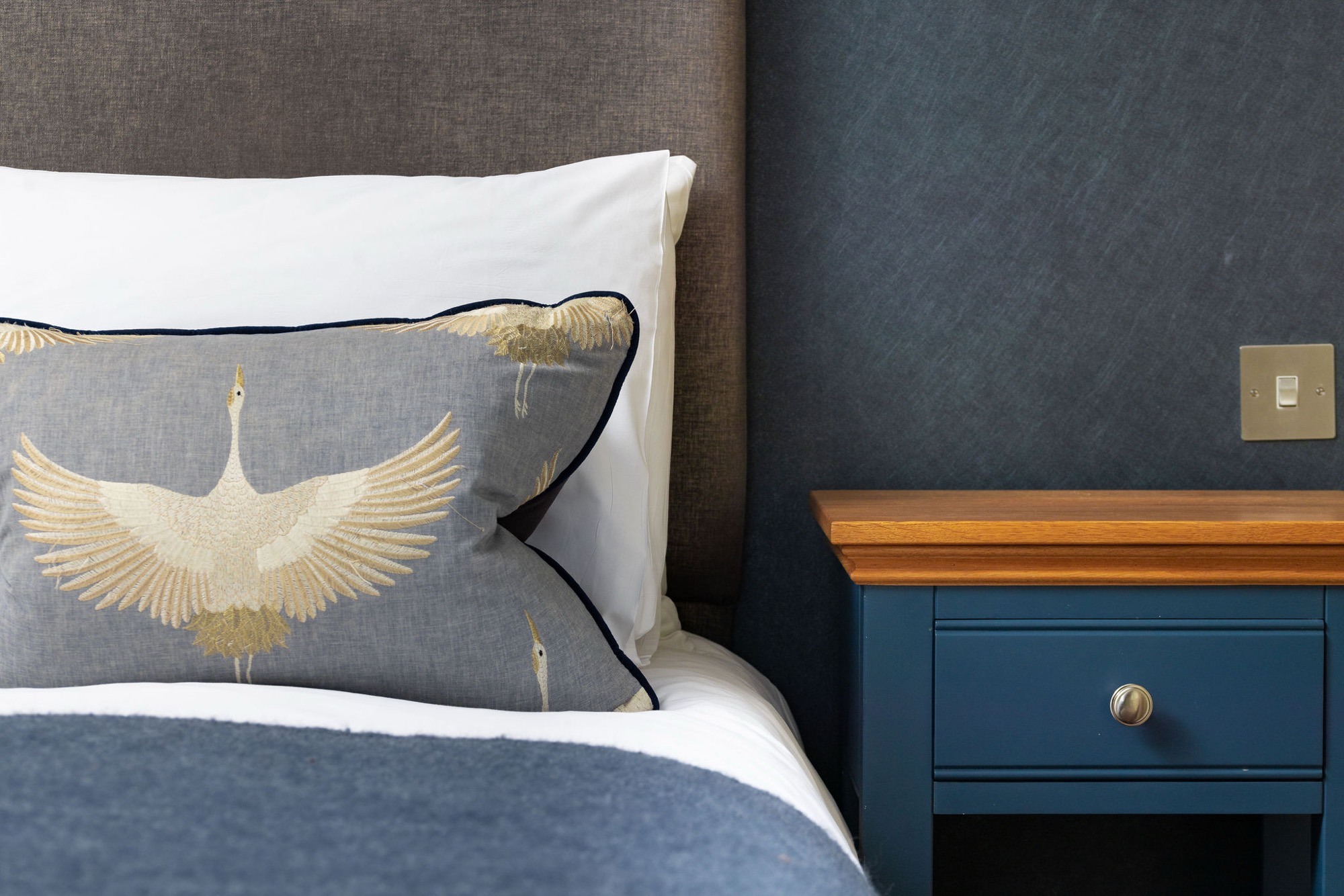A bedside detail at Ennios: gold crane embroidered pillow against navy joinery